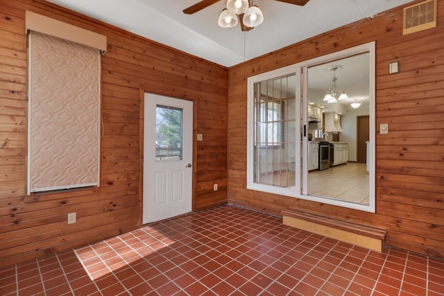 spare room featuring ceiling fan with notable chandelier, wood walls, and visible vents