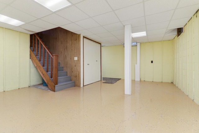 finished below grade area with concrete block wall, a paneled ceiling, and stairway