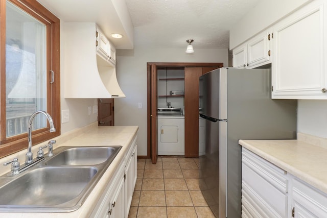 kitchen with light tile patterned floors, freestanding refrigerator, white cabinets, a sink, and washer / dryer