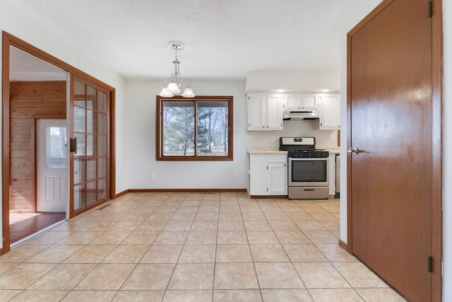 kitchen featuring light tile patterned floors, under cabinet range hood, white cabinetry, stainless steel range with gas stovetop, and an inviting chandelier