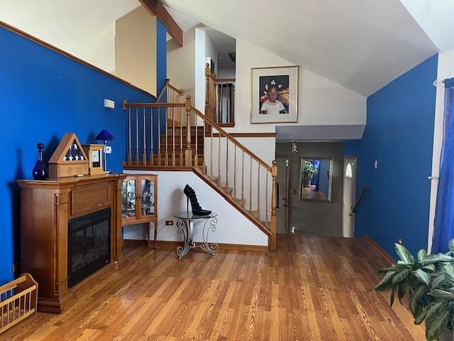 stairway with high vaulted ceiling, wood finished floors, and a glass covered fireplace