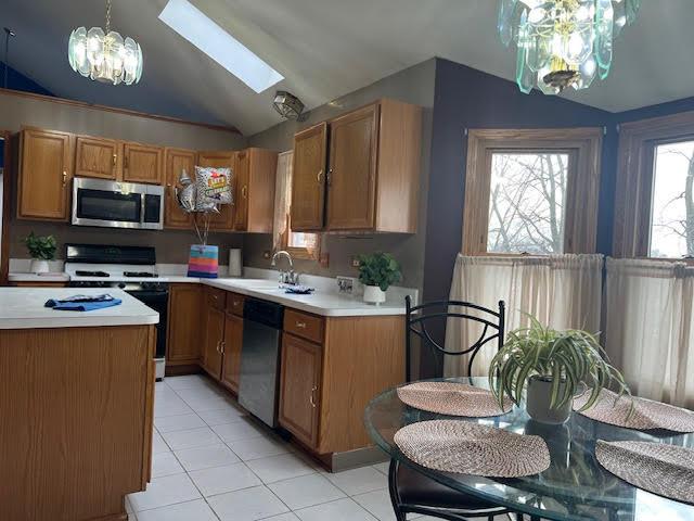 kitchen featuring a sink, vaulted ceiling with skylight, stainless steel appliances, and light countertops