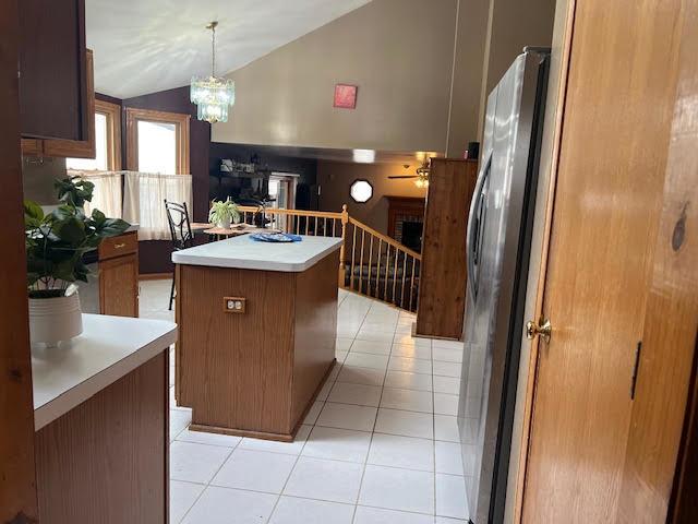 kitchen featuring brown cabinetry, a kitchen island, freestanding refrigerator, vaulted ceiling, and light tile patterned flooring