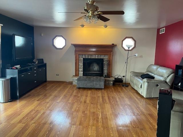 living room featuring a fireplace, visible vents, baseboards, a ceiling fan, and light wood-type flooring