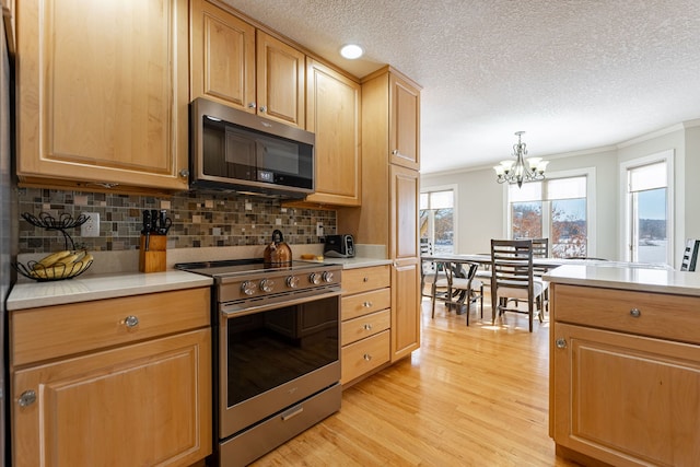 kitchen featuring pendant lighting, stainless steel appliances, light countertops, and ornamental molding