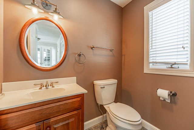 bathroom with baseboards, vanity, toilet, and a healthy amount of sunlight