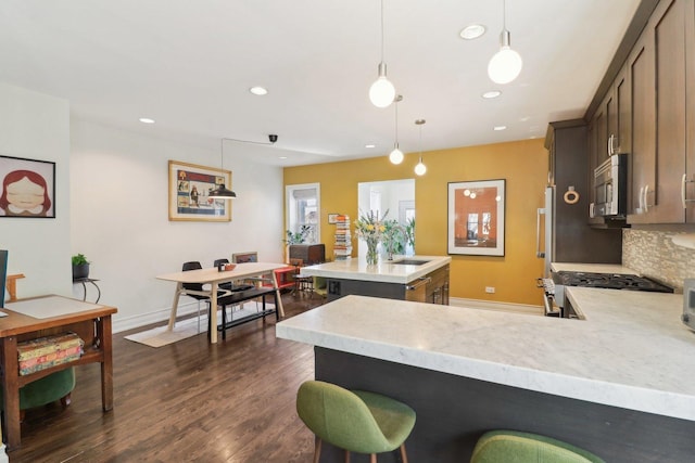 kitchen featuring dark wood-style flooring, backsplash, appliances with stainless steel finishes, a sink, and an island with sink