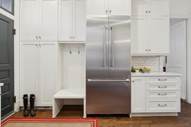 kitchen with tasteful backsplash, light countertops, built in fridge, white cabinets, and dark wood-style flooring