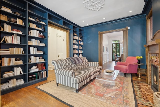 living area with built in shelves, wood finished floors, recessed lighting, a lit fireplace, and crown molding