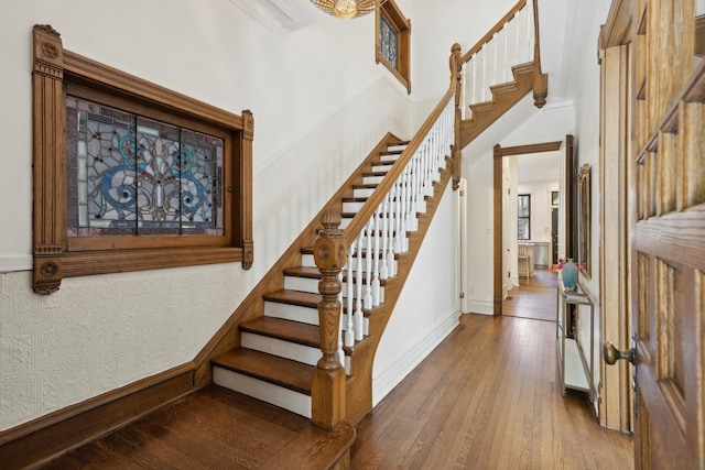 staircase with baseboards, wood-type flooring, and a towering ceiling