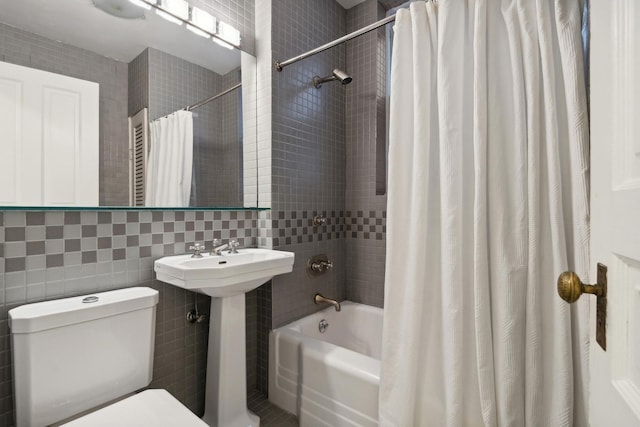 bathroom with tile walls, toilet, shower / bath combo, and a sink