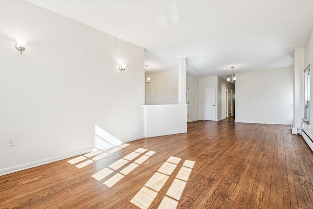 unfurnished living room featuring ornate columns, baseboards, a notable chandelier, and hardwood / wood-style flooring