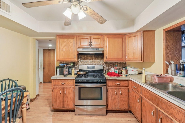 kitchen featuring visible vents, light countertops, brown cabinetry, under cabinet range hood, and stainless steel gas range oven