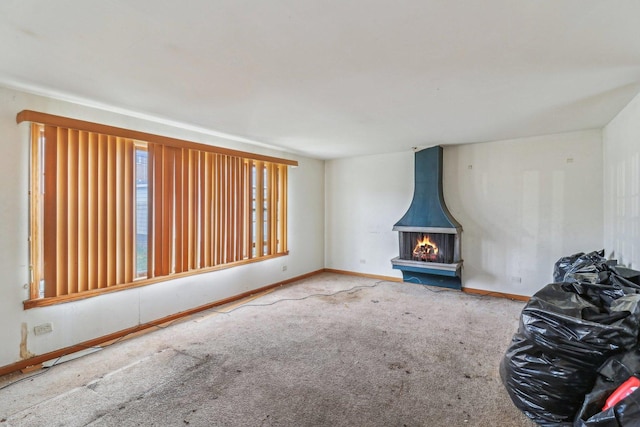 unfurnished living room with carpet floors, a wood stove, and baseboards