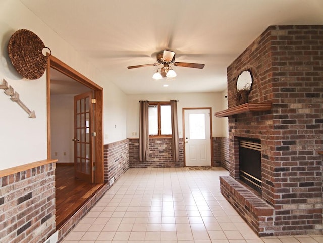 unfurnished living room with ceiling fan, brick wall, light tile patterned floors, and a fireplace