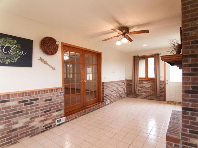 empty room featuring wainscoting, ceiling fan, brick wall, and light tile patterned floors