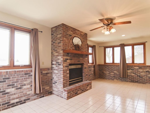 unfurnished living room featuring a ceiling fan, a brick fireplace, brick wall, and light tile patterned floors