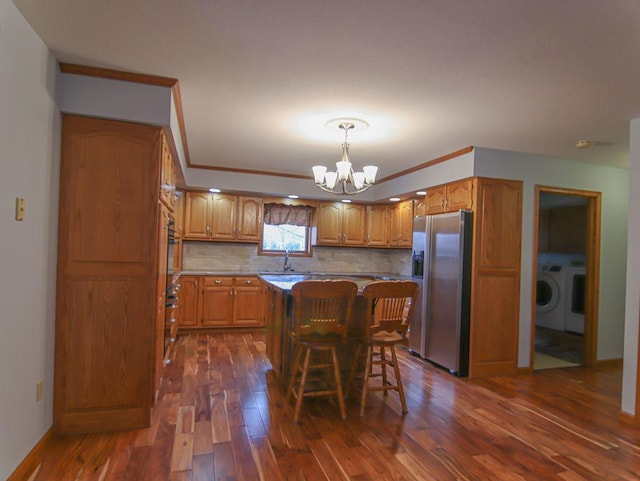 kitchen featuring a notable chandelier, a kitchen island, washer / dryer, stainless steel fridge, and a kitchen bar