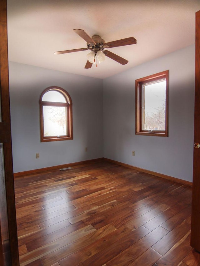 empty room featuring ceiling fan, dark wood-style flooring, and baseboards