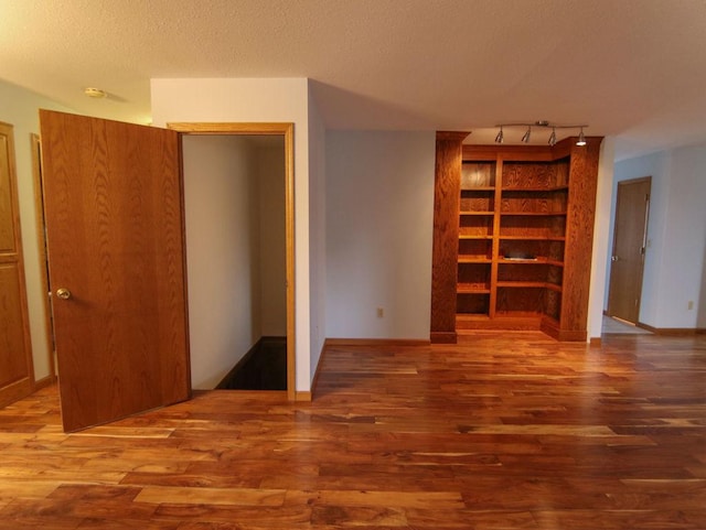 empty room featuring a textured ceiling, baseboards, track lighting, and wood finished floors