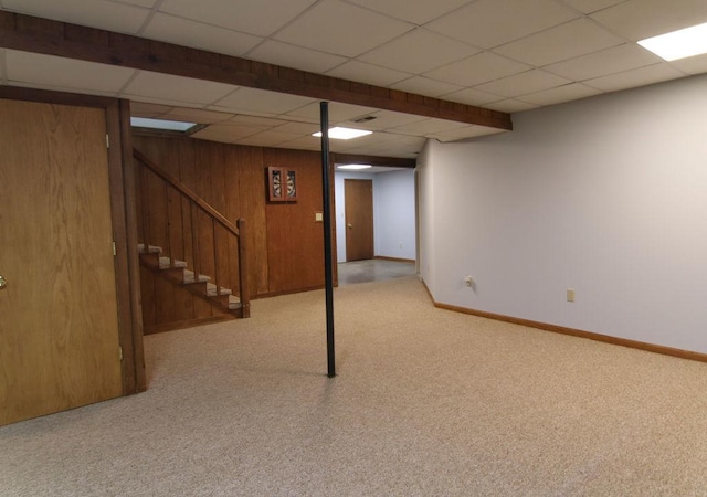 finished basement with stairs, wood walls, a drop ceiling, and baseboards