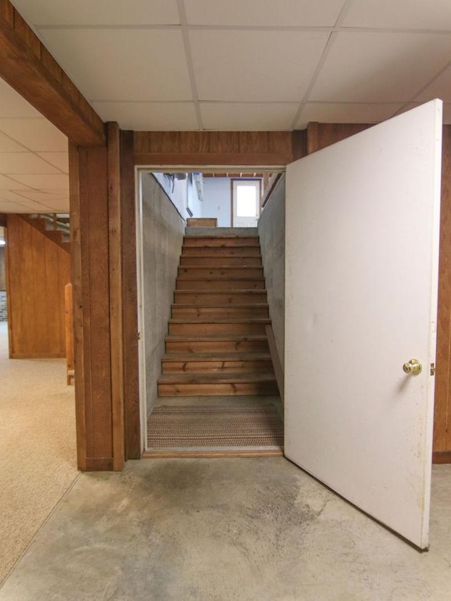 stairway featuring concrete floors, a paneled ceiling, and wooden walls