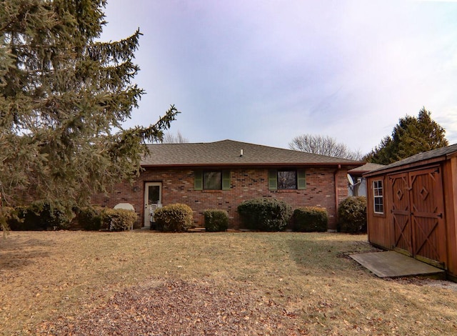 exterior space featuring brick siding, a shingled roof, a shed, an outdoor structure, and a front lawn