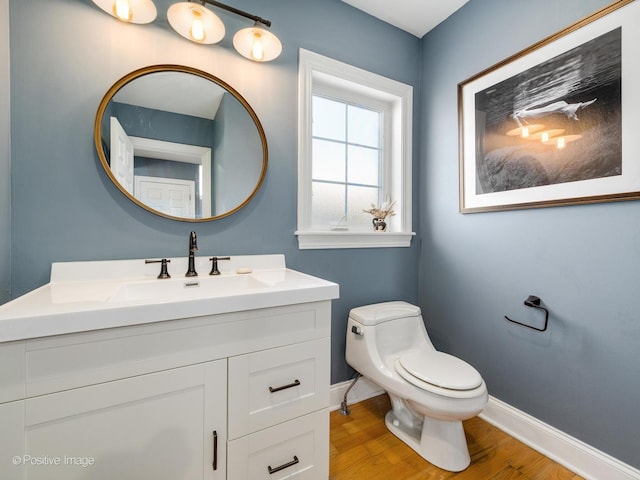 half bathroom with baseboards, vanity, toilet, and wood finished floors