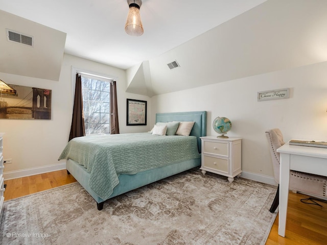 bedroom featuring lofted ceiling, visible vents, baseboards, and wood finished floors