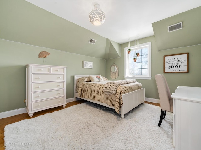 bedroom featuring lofted ceiling, visible vents, baseboards, and wood finished floors