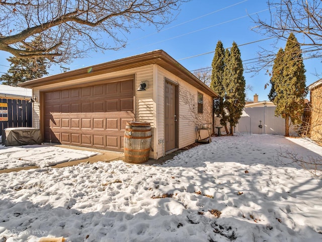 snow covered garage featuring a detached garage and fence