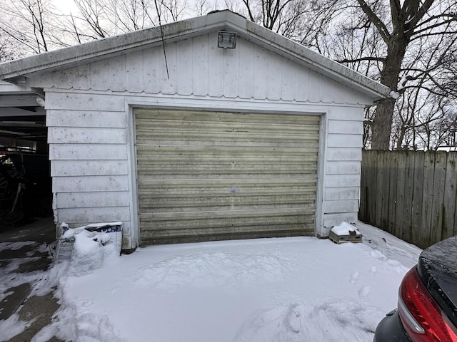 snow covered garage featuring a detached garage and fence