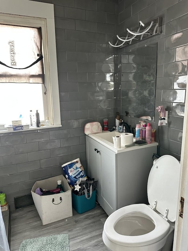 half bath with wood finished floors, a sink, toilet, and tile walls