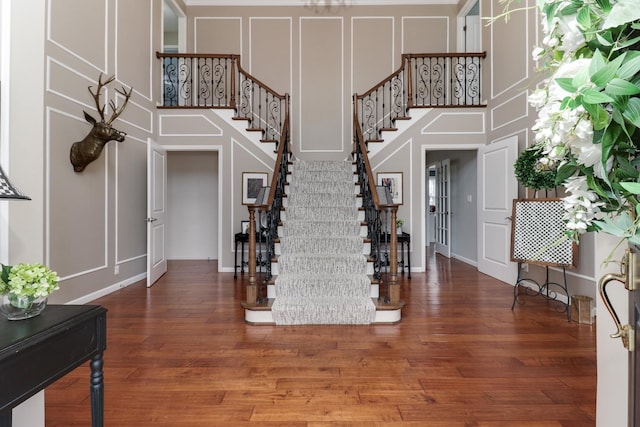 foyer entrance featuring a decorative wall, stairway, a high ceiling, and wood finished floors