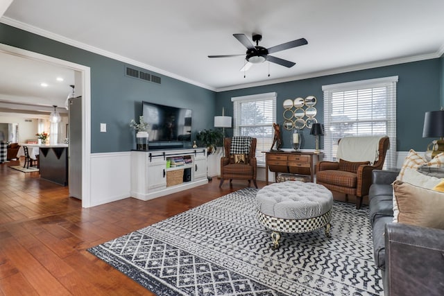 living room featuring dark wood-type flooring, visible vents, ornamental molding, and a ceiling fan