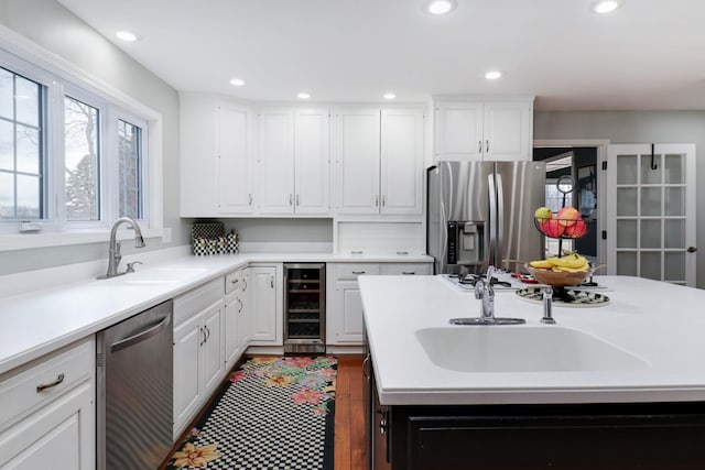 kitchen featuring beverage cooler, appliances with stainless steel finishes, a sink, and white cabinetry