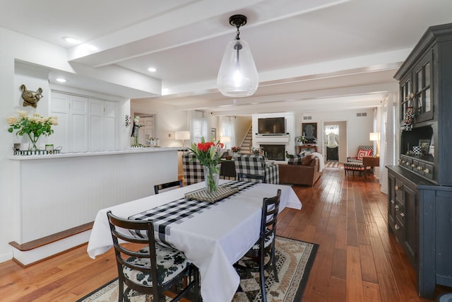 dining area featuring stairs, a fireplace, beamed ceiling, and hardwood / wood-style flooring