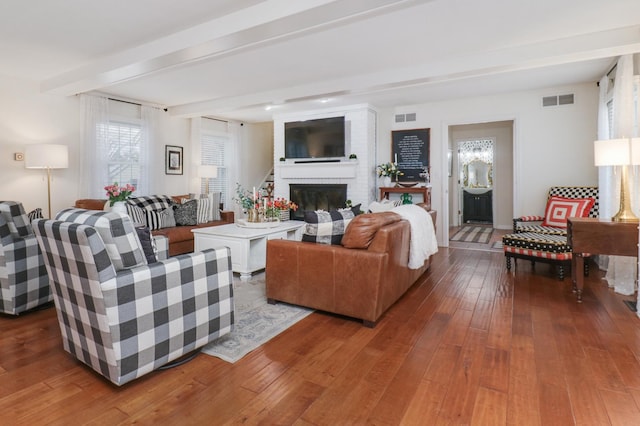 living area featuring wood-type flooring, a fireplace, visible vents, and beamed ceiling