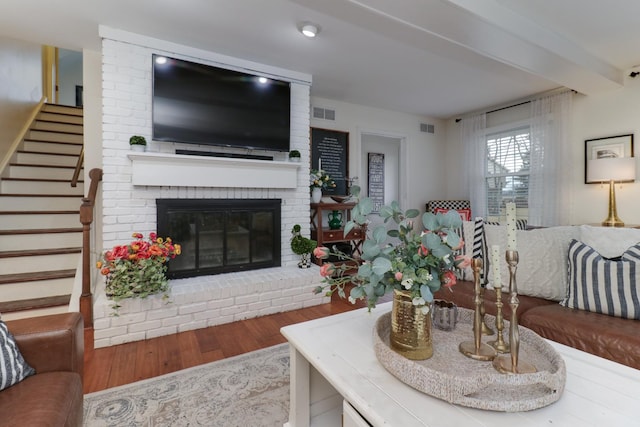 living room featuring stairway, a brick fireplace, visible vents, and wood finished floors