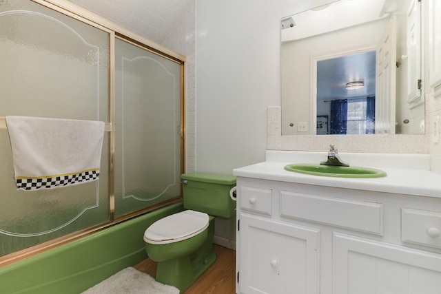 full bath with bath / shower combo with glass door, wood finished floors, vanity, and toilet