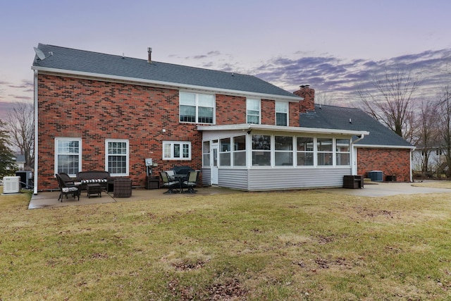 back of house at dusk featuring a sunroom, a patio area, a yard, and a chimney