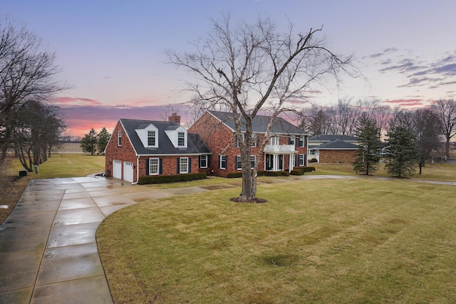 view of front facade with a front yard, a chimney, concrete driveway, and brick siding