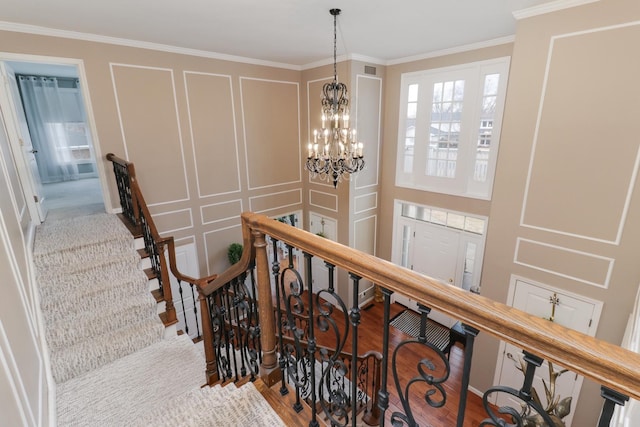 stairs with ornamental molding, a notable chandelier, and a decorative wall