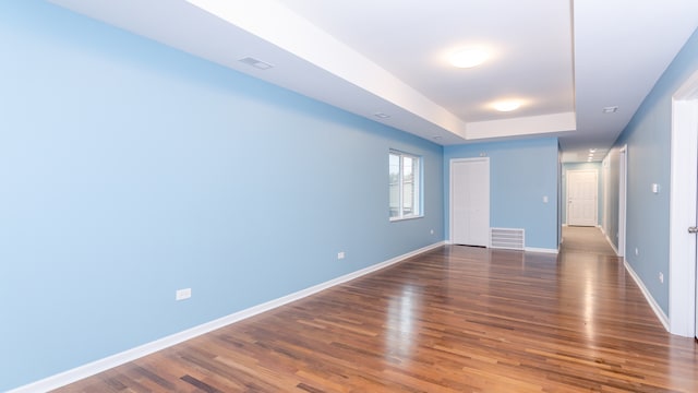 unfurnished room with visible vents, a raised ceiling, dark wood finished floors, and baseboards