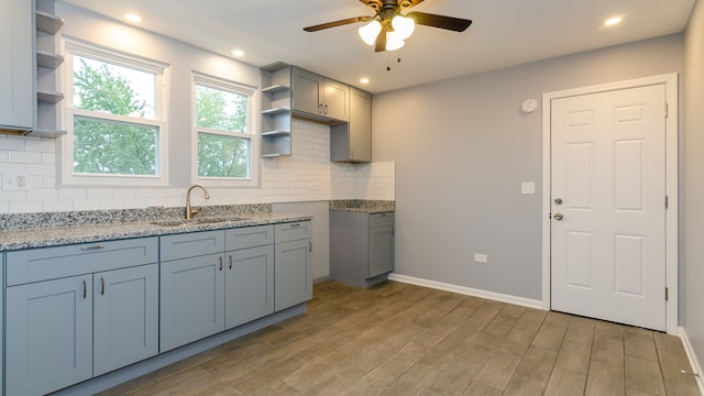 kitchen featuring open shelves, a sink, light stone countertops, and light wood-style floors