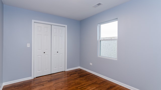 unfurnished bedroom with a closet, dark wood finished floors, visible vents, and baseboards