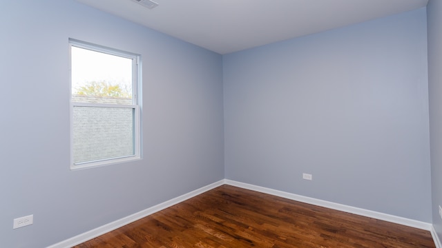 unfurnished room featuring dark wood-type flooring, visible vents, and baseboards