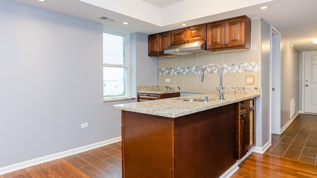 kitchen featuring light stone counters, brown cabinets, backsplash, a sink, and under cabinet range hood