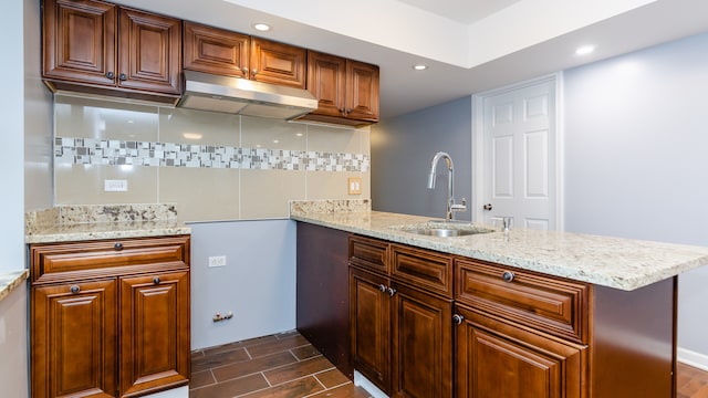 kitchen with a peninsula, under cabinet range hood, backsplash, and a sink