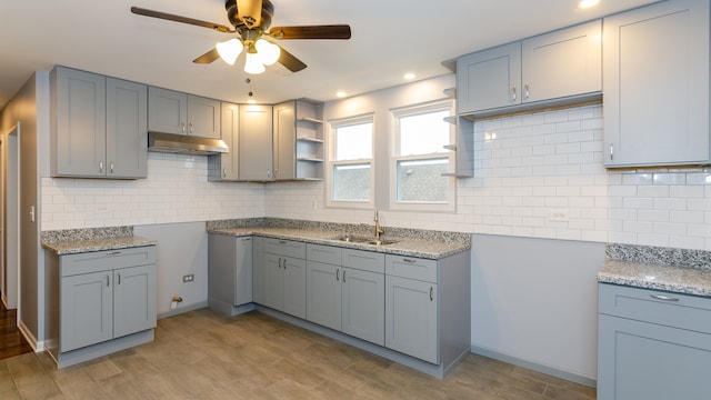 kitchen with light stone counters, gray cabinetry, under cabinet range hood, a sink, and open shelves